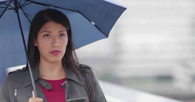 Businesswoman in city holding umbrella looking at smartphone