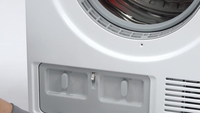 A repairman is opening the bottom part of the washing machine and he is turning the buttons for 90 degrees. He is wearing safety gloves. 