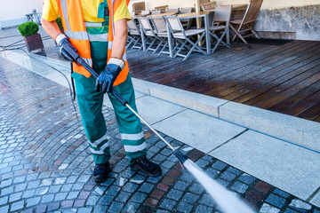 Worker cleaning the cobbled street in Ljubljana, Slovenia. - obrazy, fototapety, plakaty