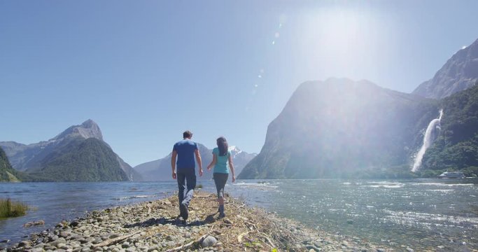 New Zealand - tourist couple hiking looking at Milford Sound enjoying iconic view and famous tourist destination in Fiordland National Park, South Island, New Zealand. Couple embracing. SLOW MOTION.