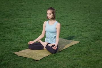 Young fit yoga  woman meditating and relaxing in lotus on the  green grass, city park background 