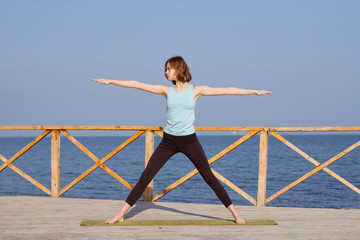 beautiful young woman  practice yoga exercise on the wooden pier, sea background 