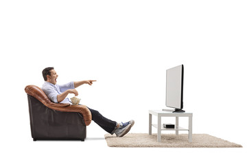 Young man seated in an armchair watching television and laughing