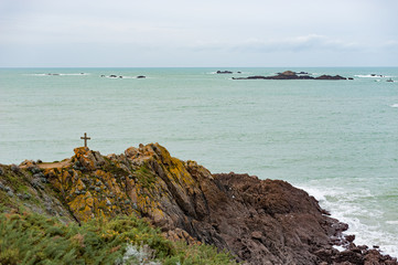 Brittany seascape with a cross on rocks and clouds on the horizon, France
