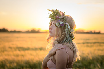 portraits of young woman having good time in wheat field during sunset, lady in head flower wreath during 