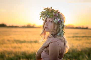 portraits of young woman having good time in wheat field during sunset, lady in head flower wreath during 