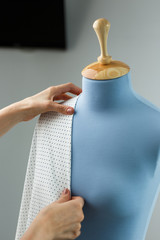 Seamstress measuring beautiful fabric on blue tailor dummy in her workshop.