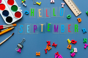 Hello September text on teacher or pupil table with school supplies side border on a blue background