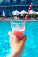 travel and vacation concept - female hand holding pink cocktail over swimming pool background