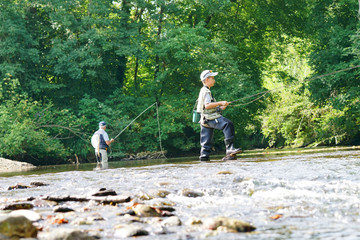 Young boy fly fishing in river, dad in background