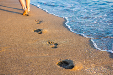 travel and vacation concept - legs, footprints in the sand and sea wave