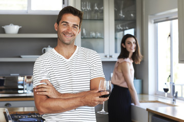 Happy guy in striped t-shirt holding wine in kitchen