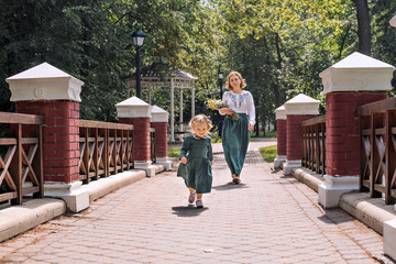  Family mom with daughter in vintage retro style linen dresses with bouquet of flowers walking  in a park garden