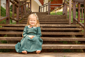 little girl in vintage retro style linen dress barefoot sitting and smiling on a wooden stairs  in the park 