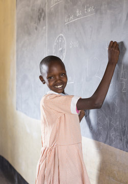 Smiling school girl using chalkboard in classroom. Kenya, Africa