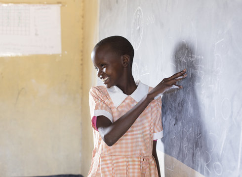 School girl using chalkboard in classroom. Kenya, Africa.