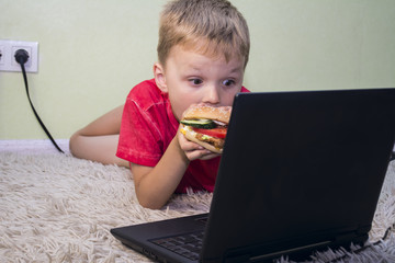 The child eats fast food and plays a laptop