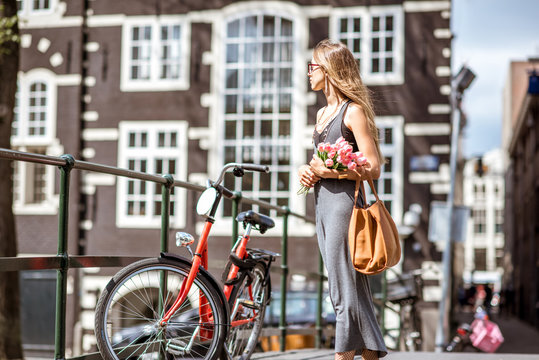 Young beautiful woman walking with bouguet of tulips on the bridge with bicycles over the water channel in Amsterdam old city