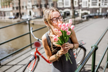 Fototapeta premium Portrait of a young beautiful woman standing with bouguet of pink tulips on the bridge in Amsterdam old city
