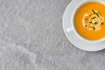 Pumpkin soup in white bowl on gray stone

