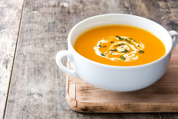 Pumpkin soup in white bowl on wooden table
