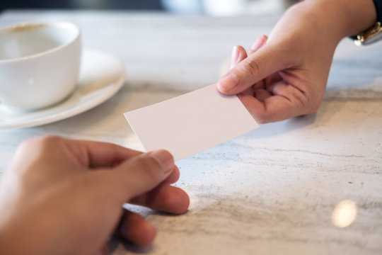 Closeup image of a business man giving a white blank business card to business woman with white coffee cup on marble table background