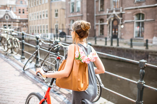 Young beautiful woman walking with bicycle holding bag and bouquet of tulips on the street near the water channel in Amsterdam old city