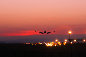 Fototapeta na wymiar Plane lands at an airfield on the background of red clouds