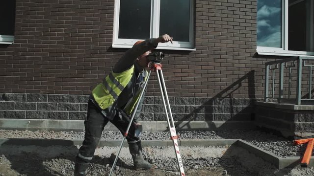 Worker in orange hard hat use theodolite and give gesture instructions to partners