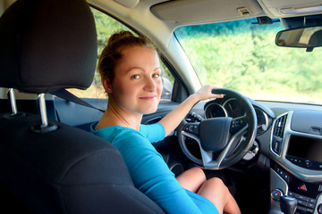 Young smiling woman in blue dress sitting in car and looking back to passengers