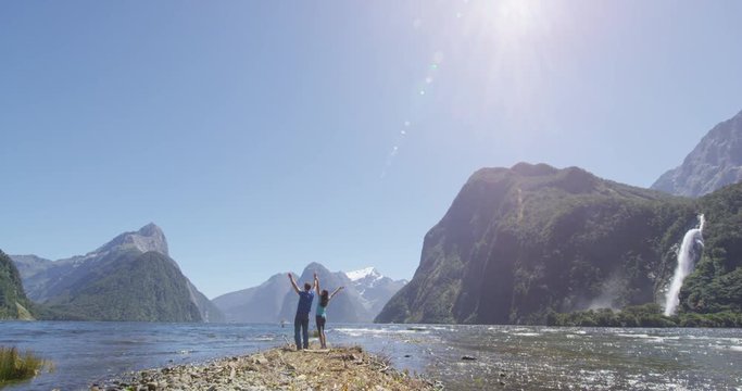 Couple celebrating jumping having fun outdoors in nature in Milford Sound, New Zealand enjoying active outdoor lifestyle hiking in Milford Sound New Zealand by Mitre Peak in Fiordland. SLOW MOTION.