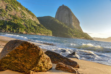 Big stones at the deserted Praia Vermelha Beach and sunrise with the bright sun illuminating the...