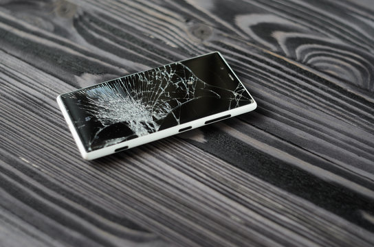 Smartphone with broken screen on dark wooden background