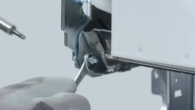 A repairman is using different repair tools to repair something on a machine. He is also wearing safety gloves. 