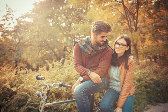 Young couple sitting on bicycle at the park on autumn day.Love and making fun.