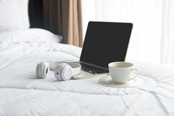 The laptop working on the white bed and coffee in the sunny day morning holiday.  Lifestyle Concept. soft and select focus