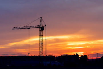 Fototapeta na wymiar Industrial construction cranes and building silhouettes over sun at sunrise. Background with copy space area for a text.