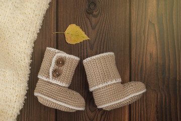 hand made crochet baby booties and Autumn fallen multi-colored leaves on wooden background, toned photo