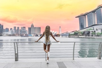 Girl with long golden hair stands on the bridge and looks at a beautiful sunset in the city of Singapore
