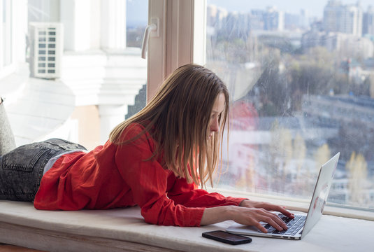 Yuong pretty woman with cellphone sitting on the window sill, caucasian famele using smartphone 