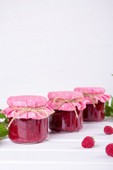 Jars with raspberry jam placed in rows and fresh raspberry on white wooden table