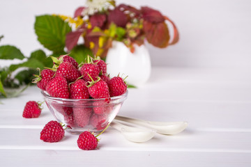 Red fresh raspberries in a glass bowl with green leaves on white background. 