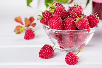 Red fresh raspberries in a glass bowl with green leaves on white background. 