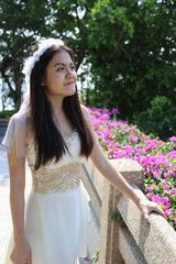 asian woman who wear white crown and ballet dress has little smile look at right side in the garden
