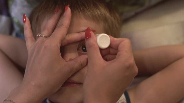 Mom drips eye drops to son. Mother drips son in eye medical solution