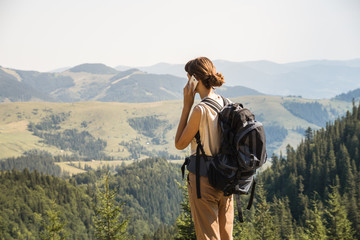 Young female backpacker uses mobile phone to communicate in rural mountain area of ukrainian carpathian mountains. Girl with tourist rucksack on a long hiking walk talks on smartphone up in the hills