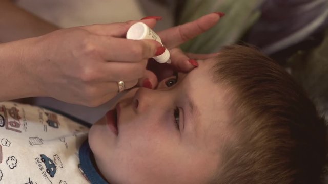 Mother drips her son in eye medical solution. Healthy care concept