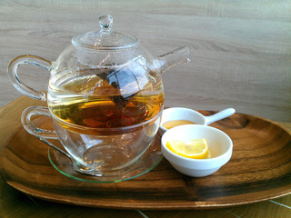 Green hot tea on a teapot and sliced lemon on a wooden background.