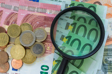 magnifying glass on pile of Euro banknotes with Euro coins as financial analysis concept