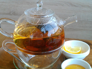 Green hot tea on a teapot with sliced lemon on a wooden background.